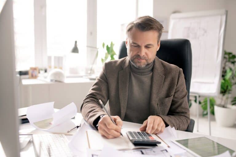 Mature engineer or accountant with pen and calculator making notes in notebook